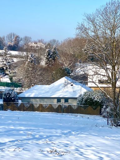 IN VERSCHNEITER UMGEBUNG Schneebedecktes Haus in einer winterlichen Landschaft mit Bäumen im Hintergrund.