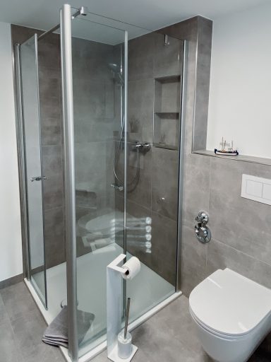 BODENTIEFE DUSCHE Moderne Badezimmer mit verglaster Dusche und WC, grauen Fliesen und Handtuchhalter.