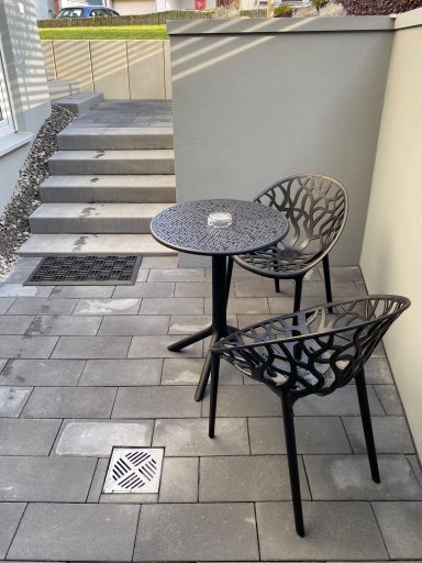 KLEINE TERRASSE Zwei moderne Stühle und ein kleiner Tisch auf einem gepflasterten Außensitzbereich.